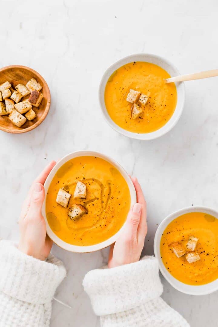 eine hand hält eine schale vegane karottensuppe