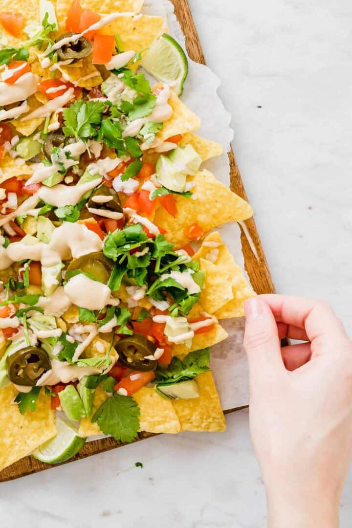 a hand grabbing vegan nachos