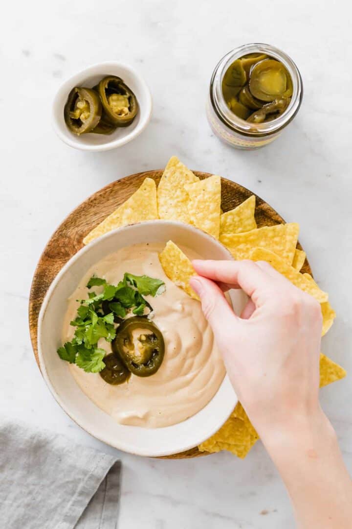 a hand dipping a tortilla chip into vegan queso