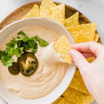 eine hand dippt ein tortilla chips in vegane käsesauce