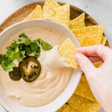 eine hand dippt ein tortilla chips in vegane käsesauce