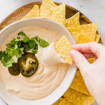 eine hand dippt ein tortilla chips in vegane käsesauce