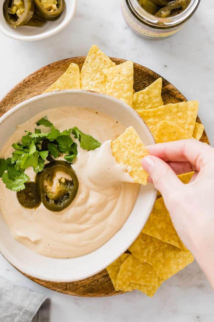 eine hand dippt ein tortilla chips in vegane käsesauce