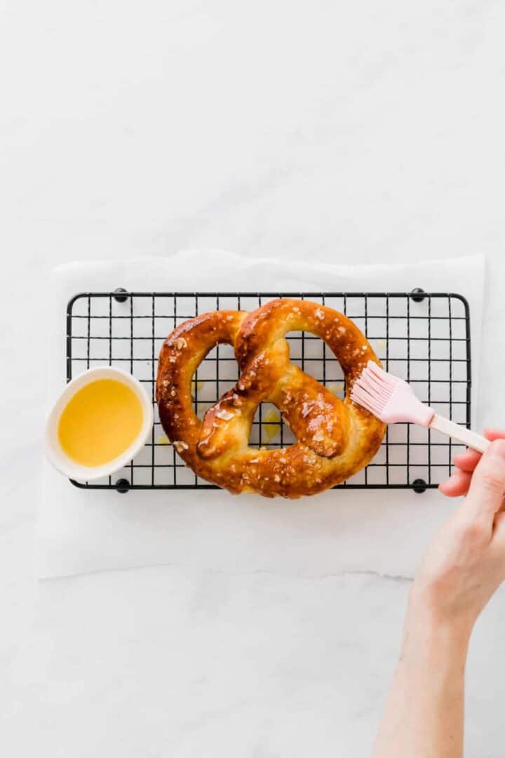 a hand brushing a freshly baked pretzel with butter