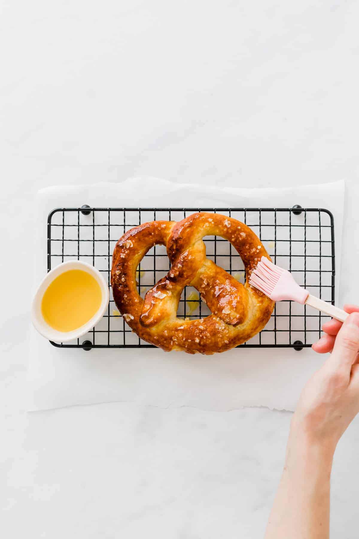 eine hand bestreicht die brezel mit flüssiger butter