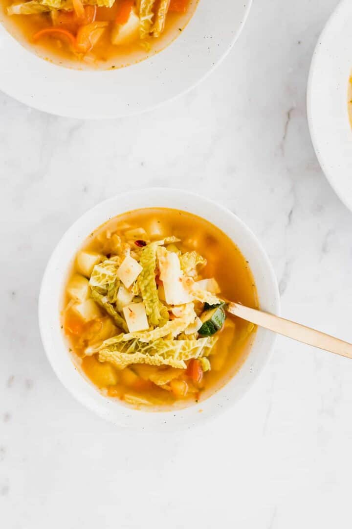 mixed vegetable soup served in a bowl with a golden spoon