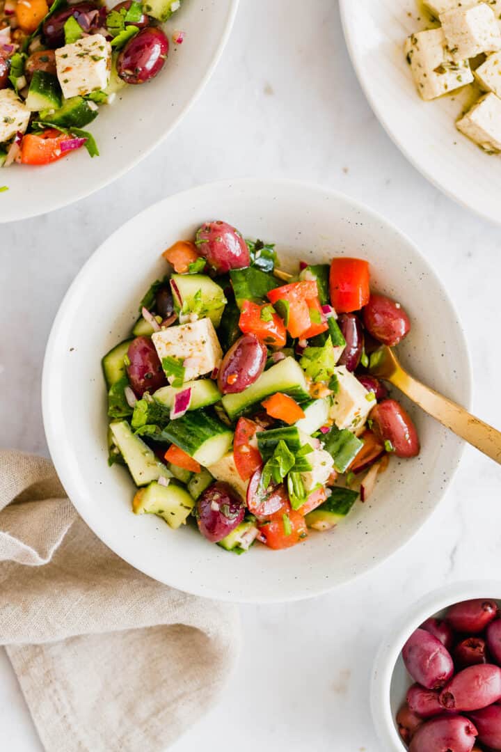 vegan greek salad served in a small bowl with a golden fork