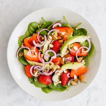 strawberry spinach salad with avocado, toasted almonds, and onions in a bowl