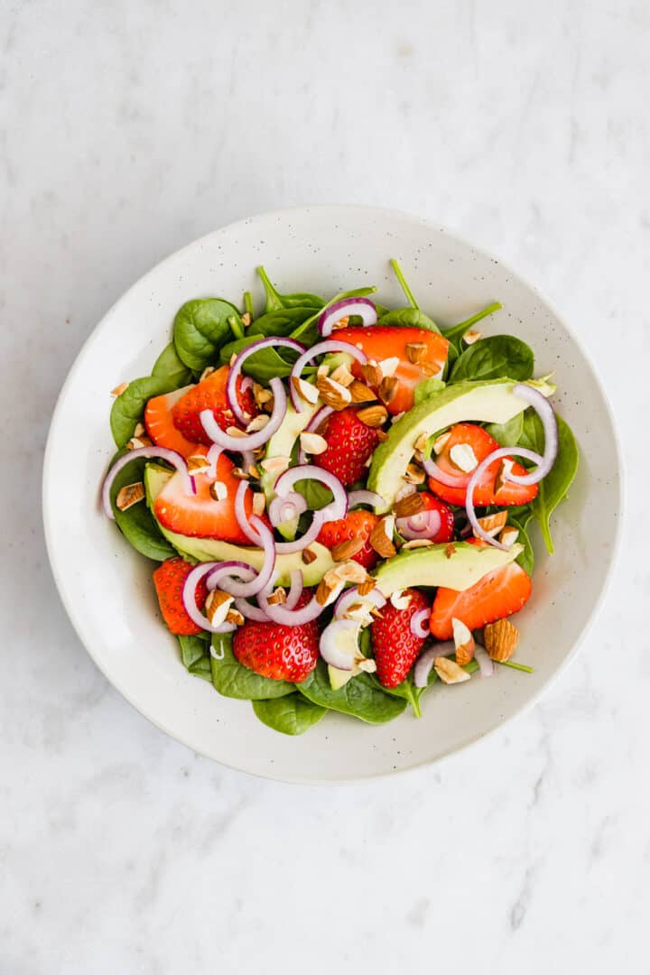 spinach, strawberry, avocado, toasted almonds, and onions in a bowl