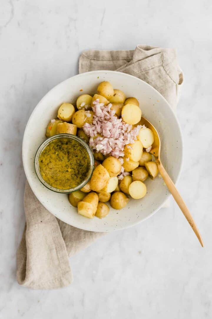 a bowl with cooked potatoes, dressing, and chopped shallots