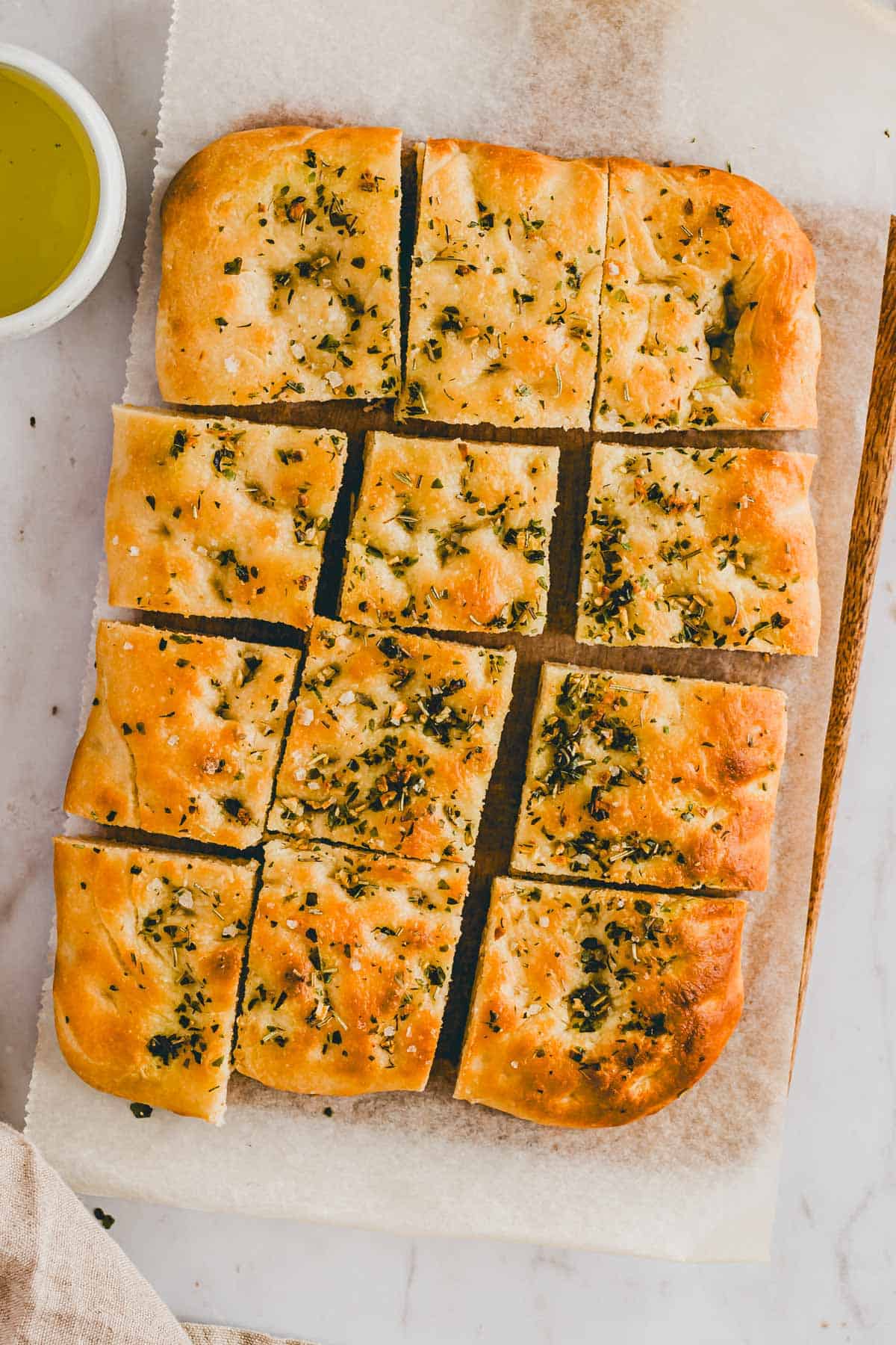 geschnittene focaccia mit kräutern neben einem schälchen olivenöl