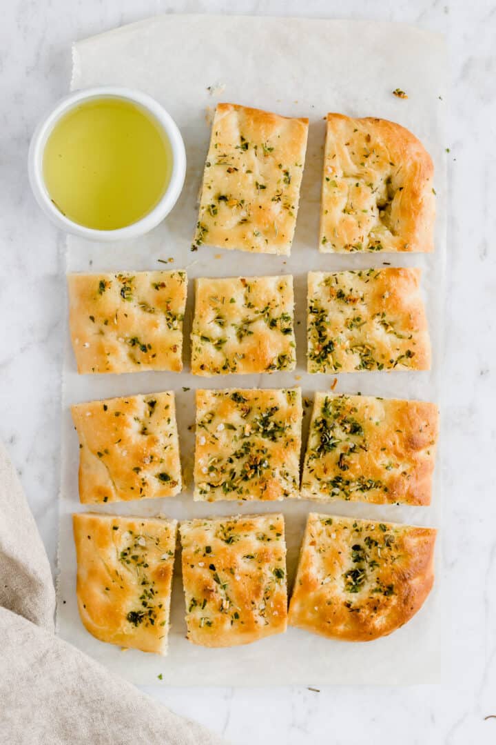 a sliced focaccia bread on a table next to a bowl with olive oil