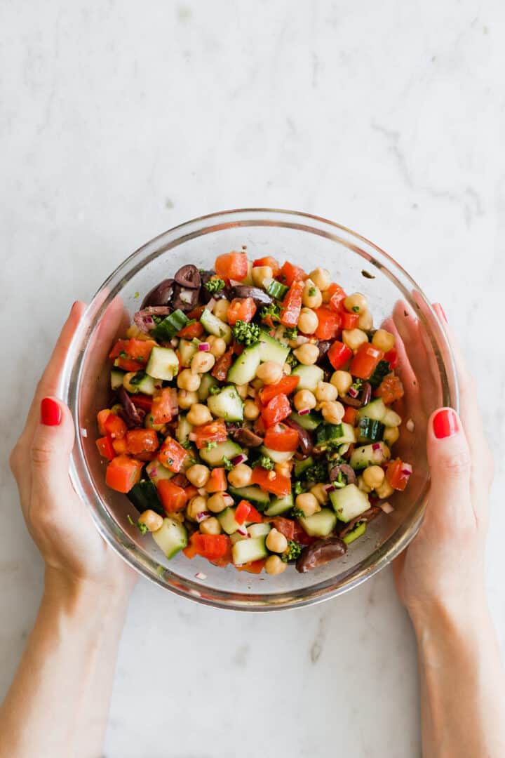 two hands holding a glass bowl filled with salad