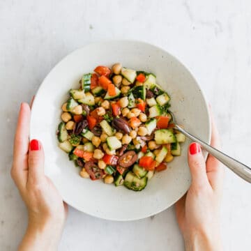 two hands holding a plate with greek chickpea salad