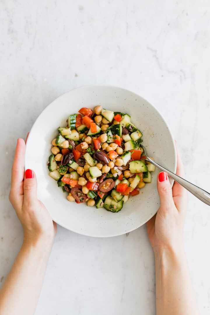 two hands holding a plate with greek chickpea salad