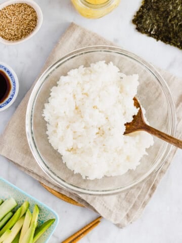 cooked sushi rice in a glass bowl next to sushi ingredients