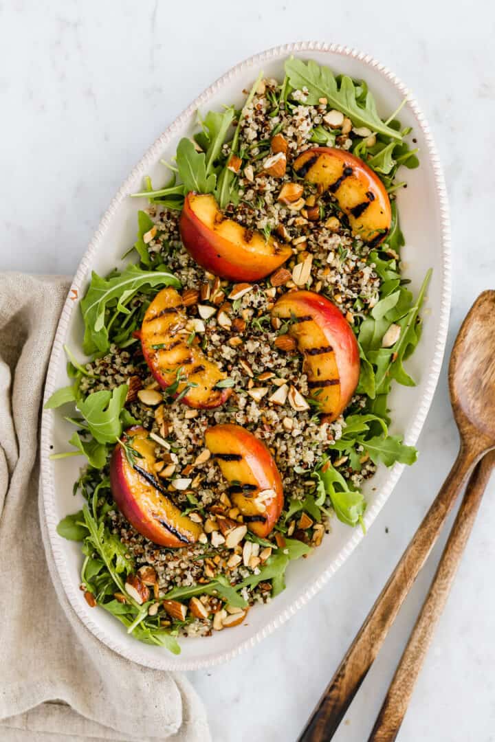 eine servierplatte mit quinoa salat, gegrilltem pfirsich, und rucola