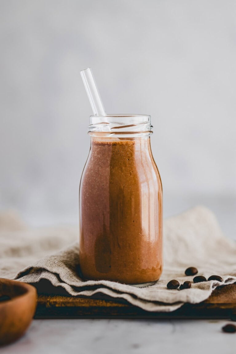 eine kleine glasflasche gefüllt mit kaffee smoothie und einem glasstrohhalm