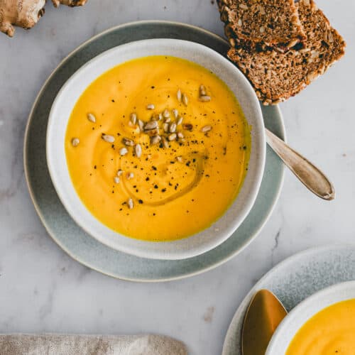 carrot ginger soup in two bowls with slices of bread