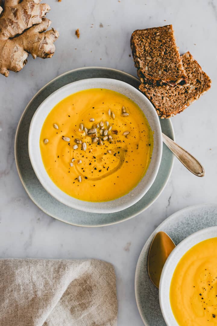 carrot ginger soup in two bowls with slices of bread