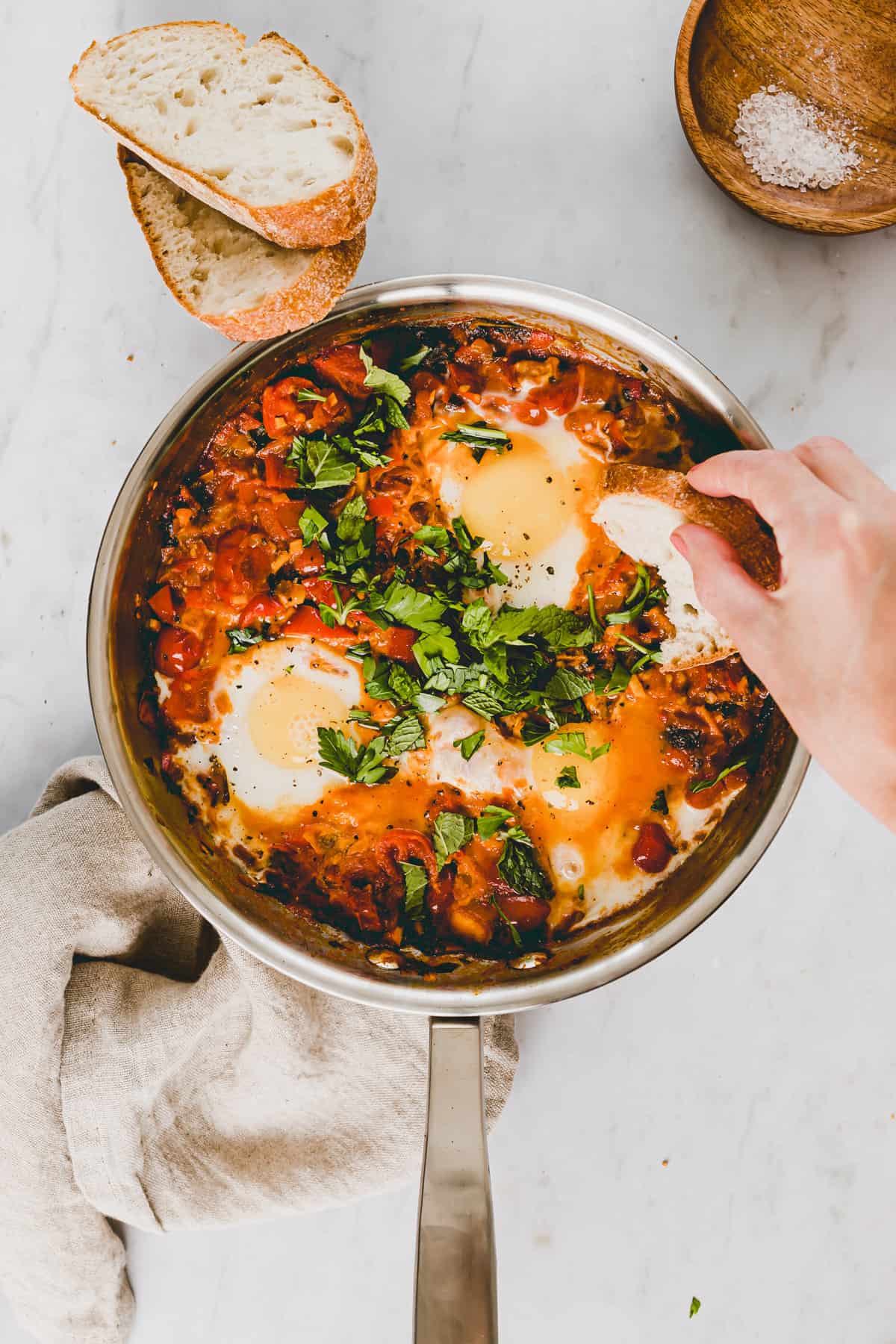a hand dipping a bread into a skillet of homemade shakshuka