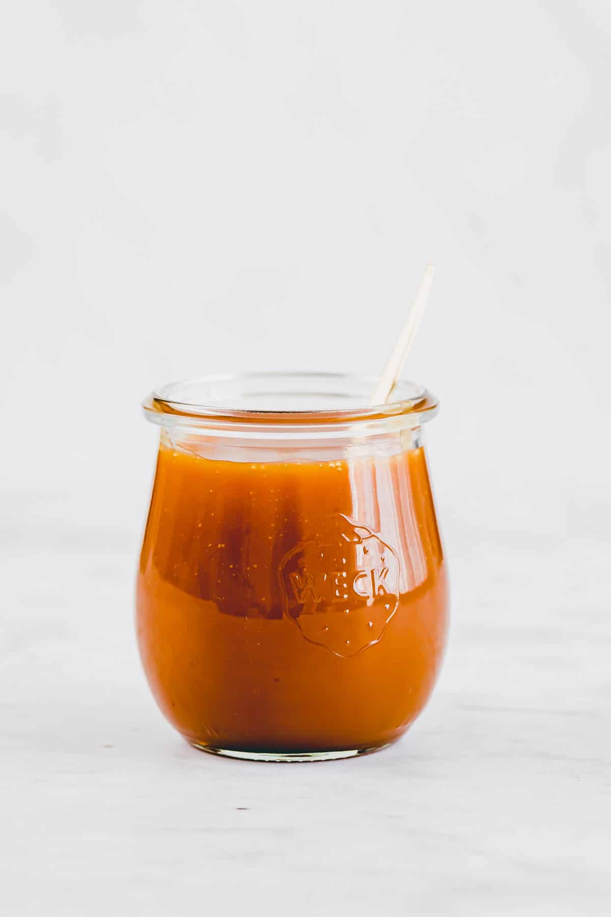 a jar filled with homemade caramel sauce and a golden spoon