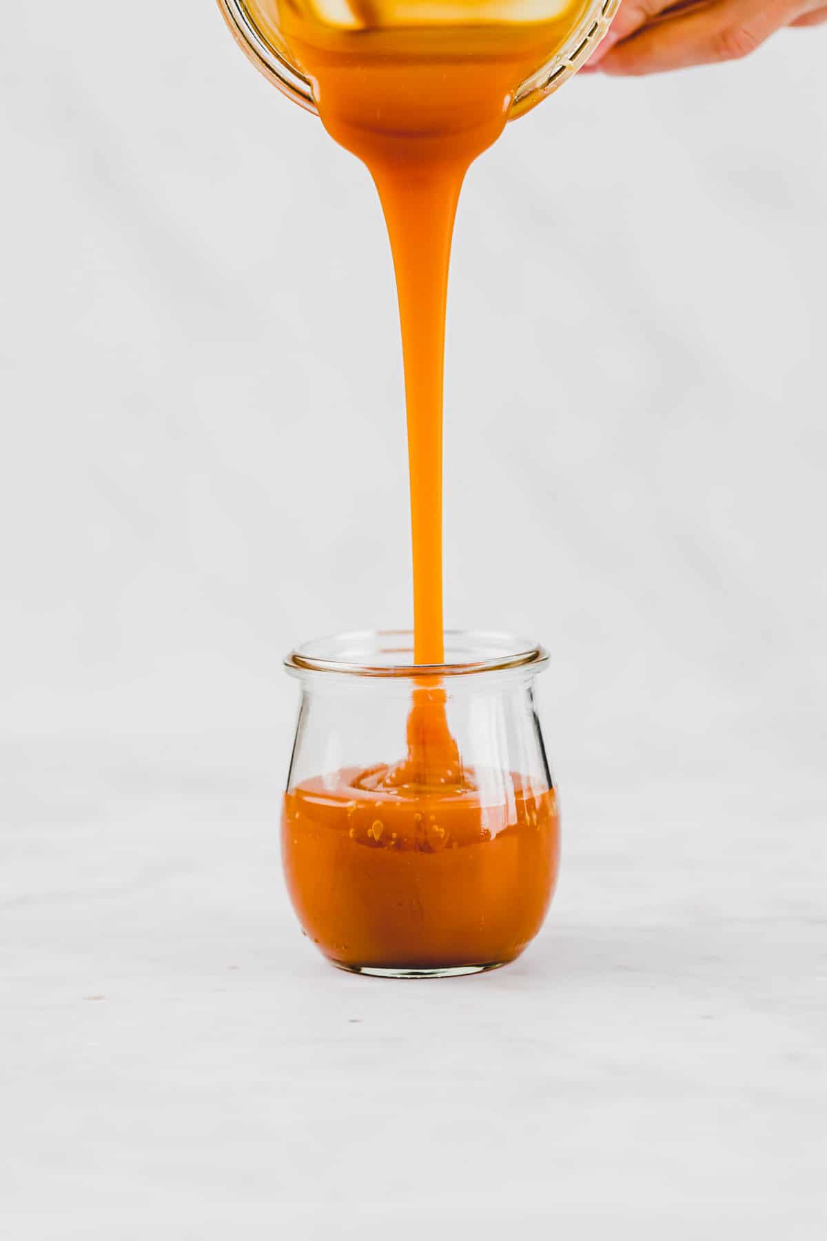 pouring dairy-free caramel sauce into a tulip jar