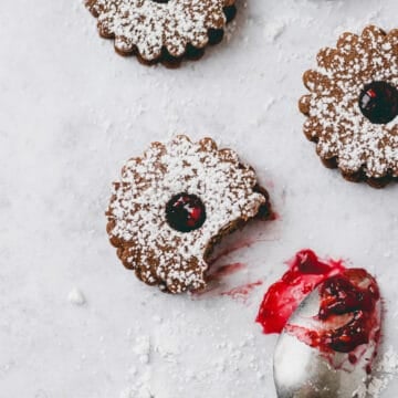 chocolate linzer cookies next to a teaspoon with raspberry jam