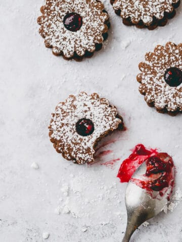 chocolate linzer cookies next to a teaspoon with raspberry jam