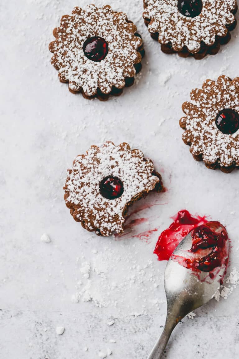 chocolate linzer cookies next to a teaspoon with raspberry jam
