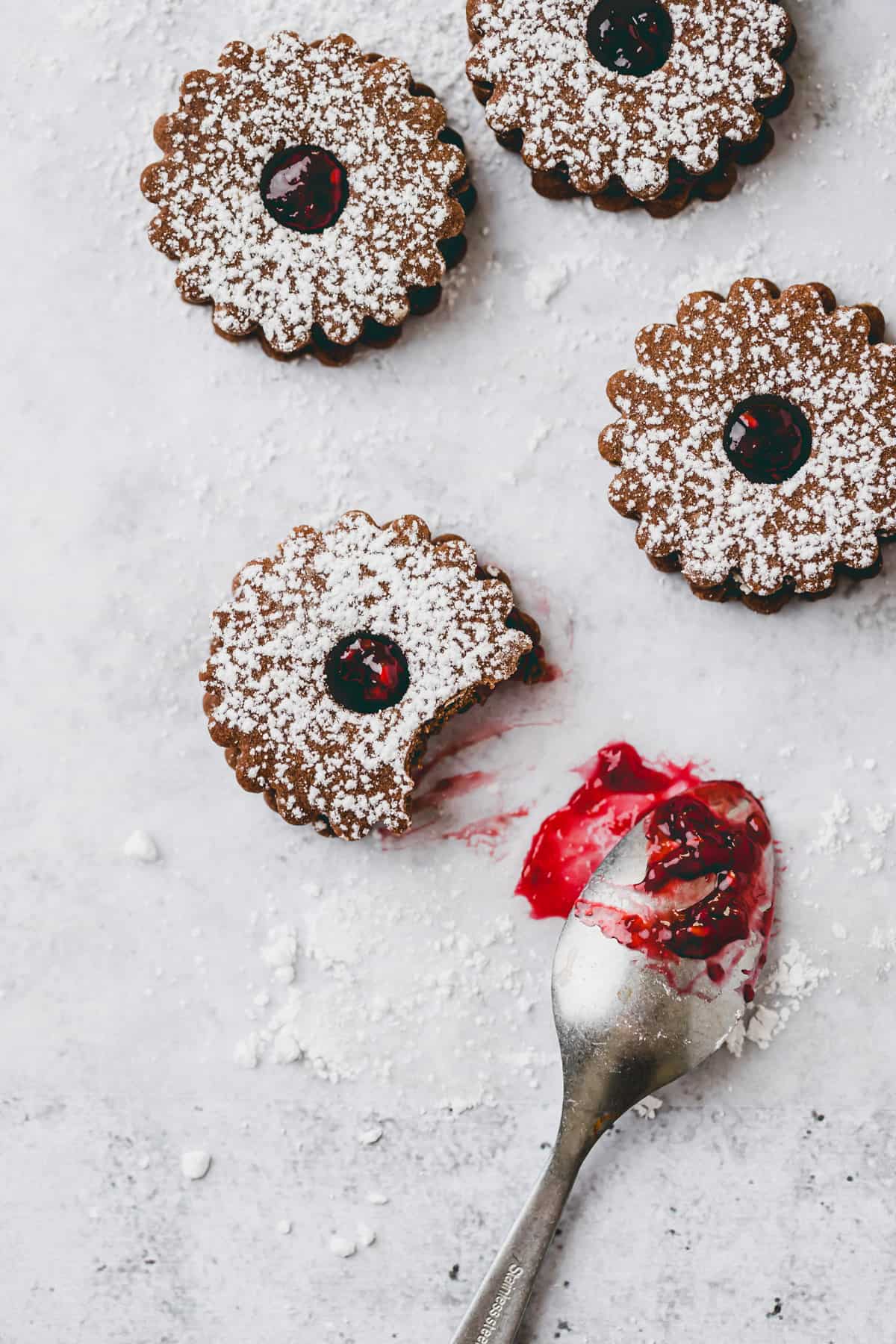 chocolate linzer cookies next to a teaspoon with raspberry jam