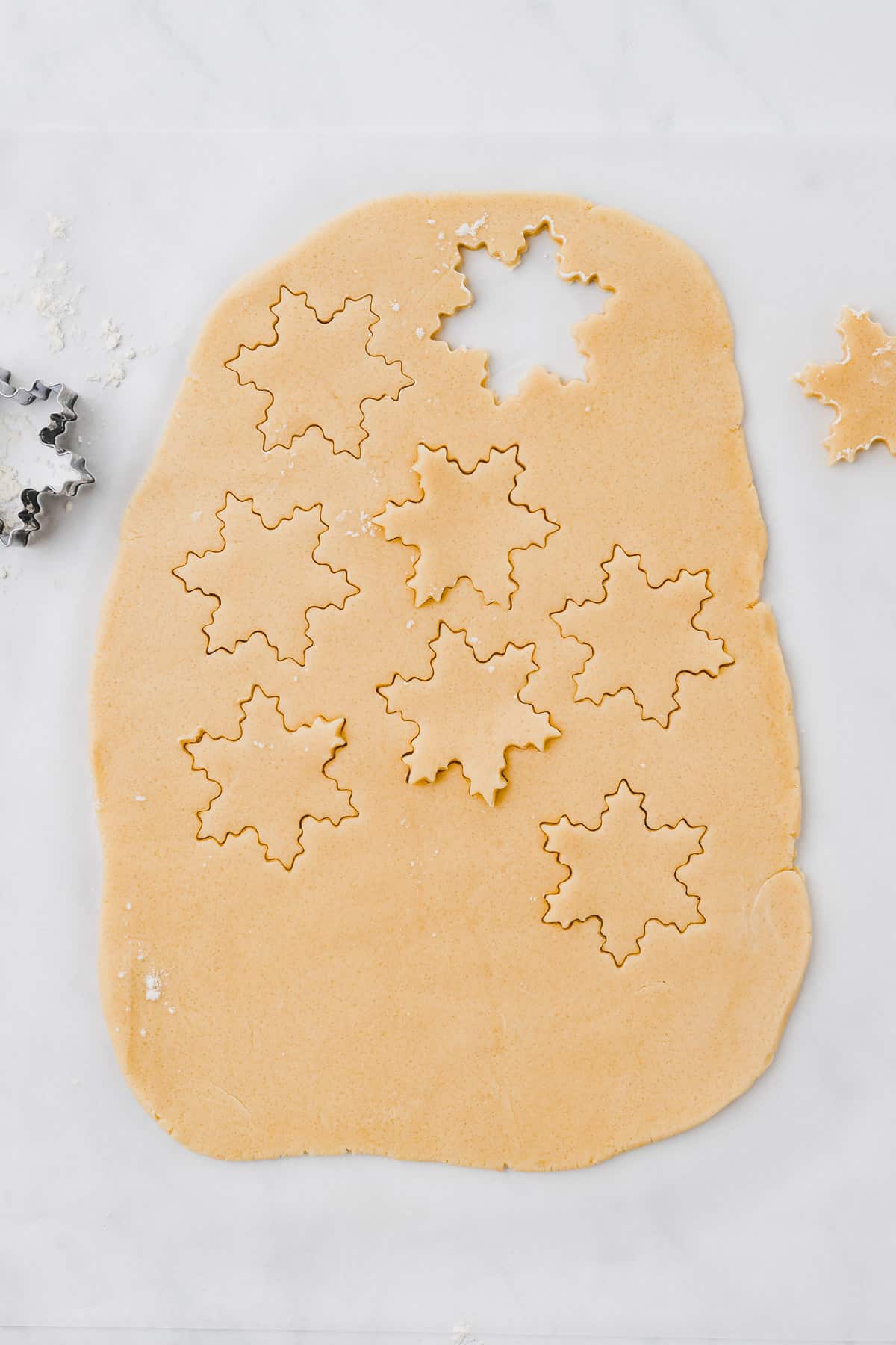 rolled out sugar cookies dough with a snowflake cookie cutter