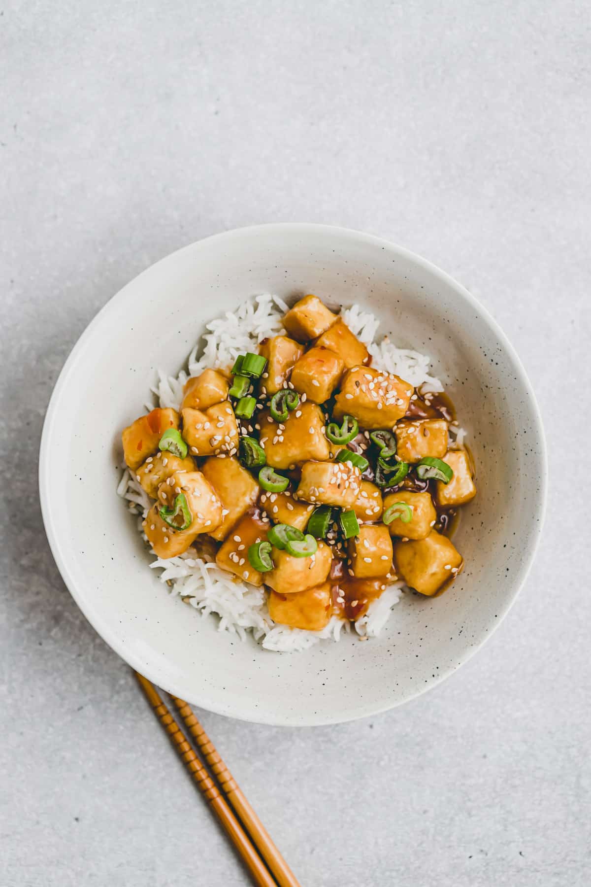 vegan orange chicken in a bowl served with rice, sesame, and scallions