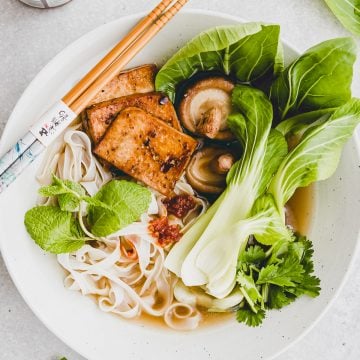 vegane pho in einem suppenteller neben pak choi und frischer minze