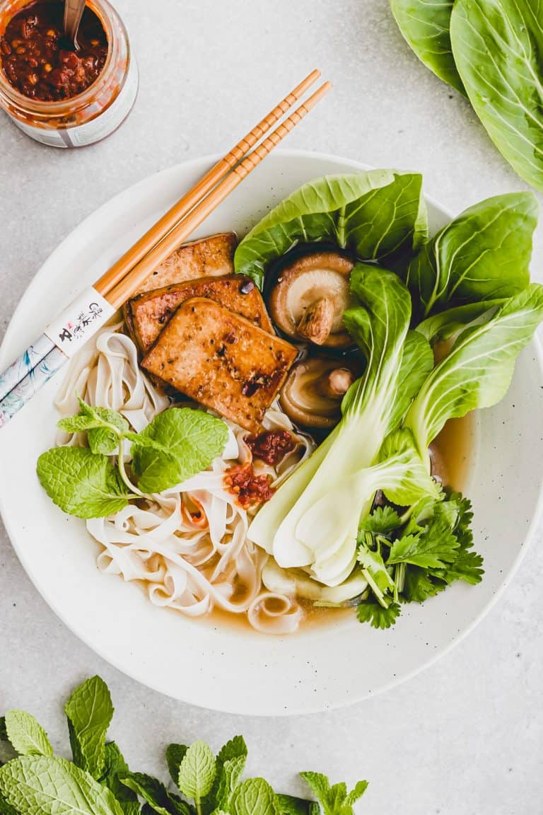 vegane pho in einem suppenteller neben pak choi und frischer minze