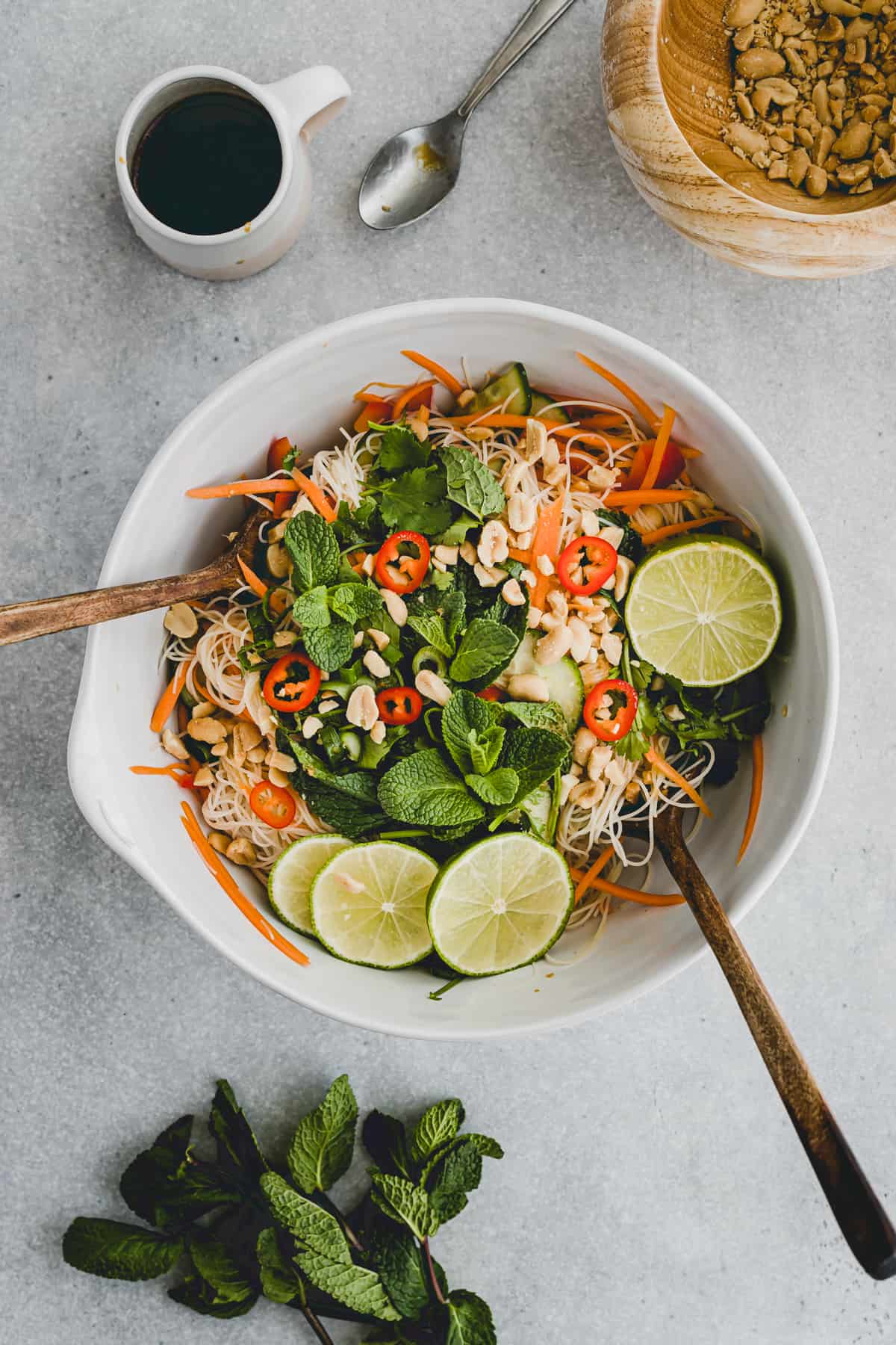 asian vegan vermicelli noodle salad in a bowl next to herbs, dressing, peanuts