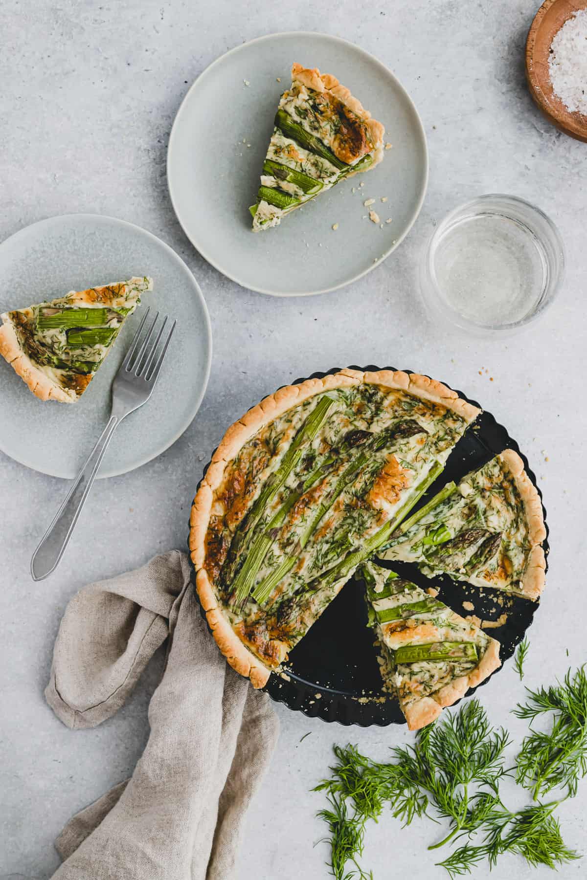 sliced quiche with green asparagus in a quiche pan next to two slices of quiche on a plate