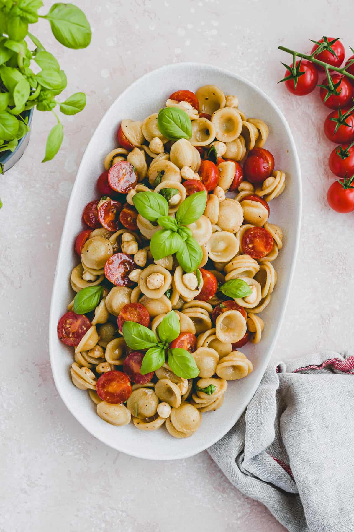 caprese pasta salad next to cherry tomatoes and fresh basil