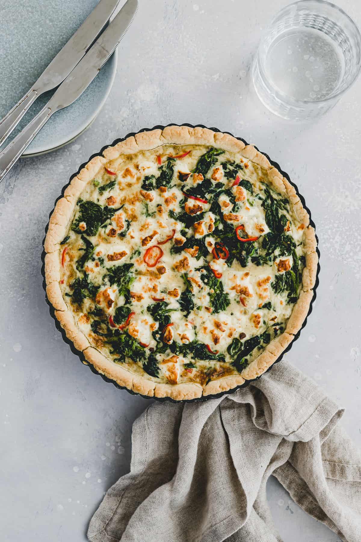 spinach feta quiche next to a glass of water and two plates