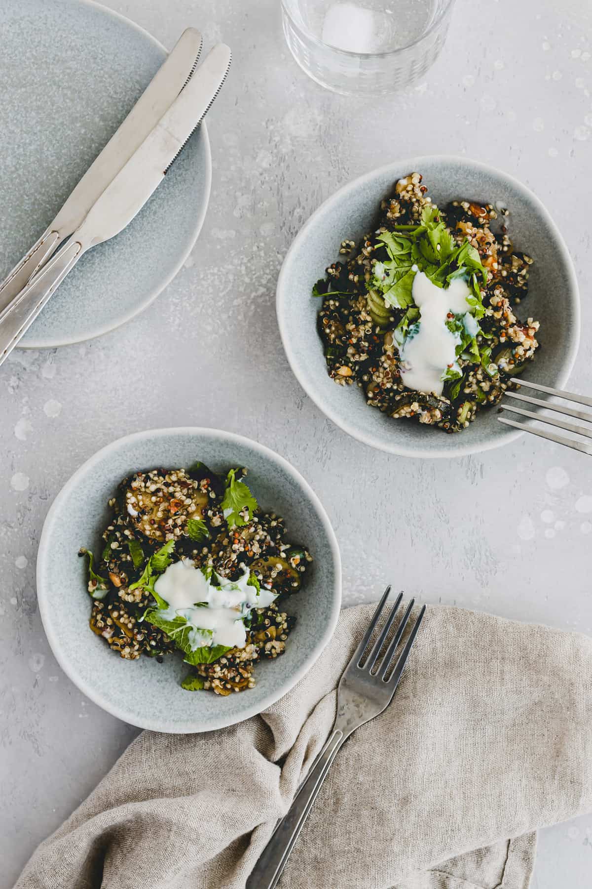 summer quinoa salad with zucchini and apricots in two bowls next to a glass of water