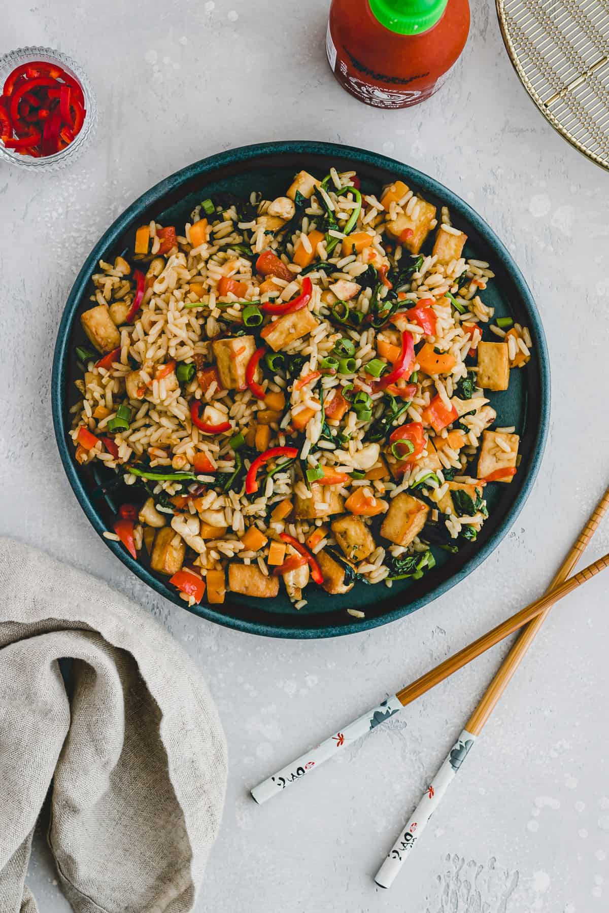 Gebratener Reis mit Gemüse und Tofu neben einer flasche sriracha