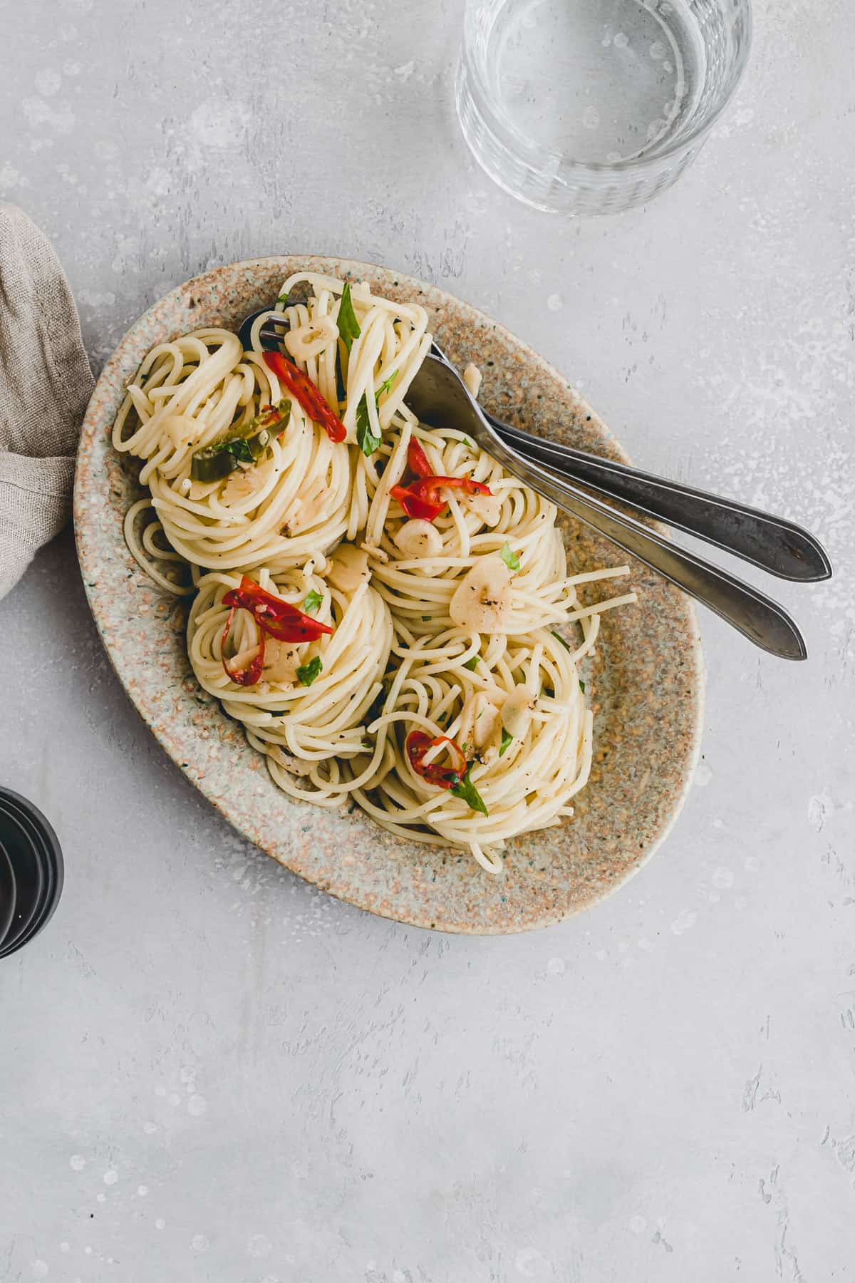 spaghetti aglio e olio on a brown plate with cutlery