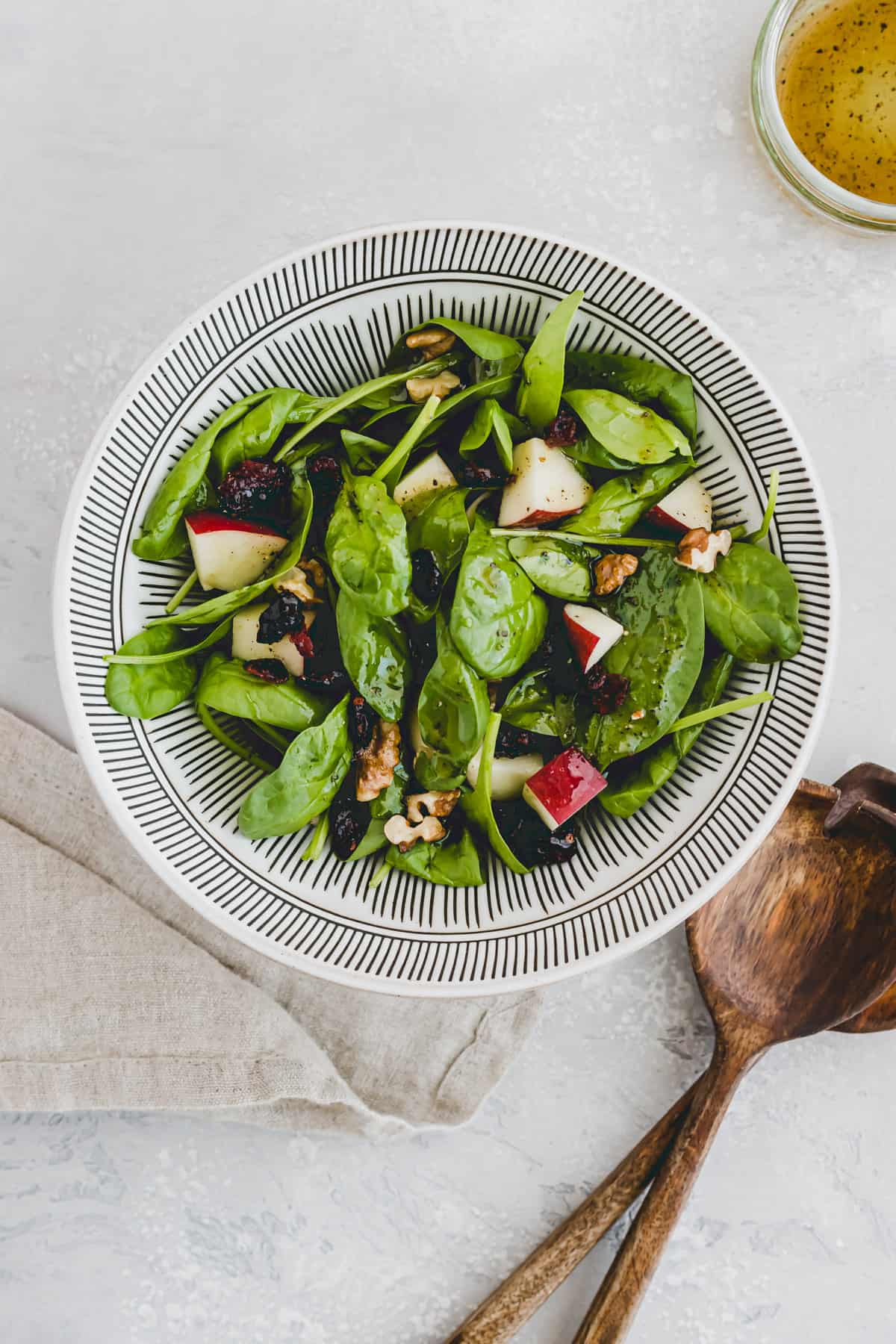 Spinach Salad with Apple, Cranberry & Walnut next to a glass vinaigrette