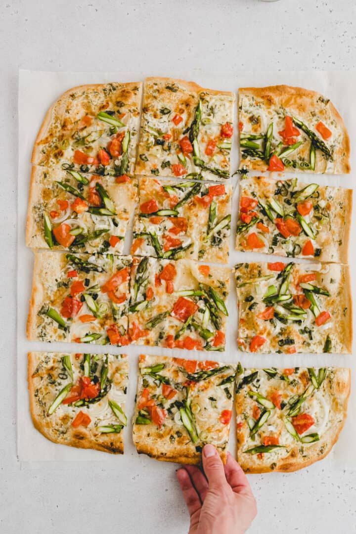 eine hand greift nach spargel flammkuchen
