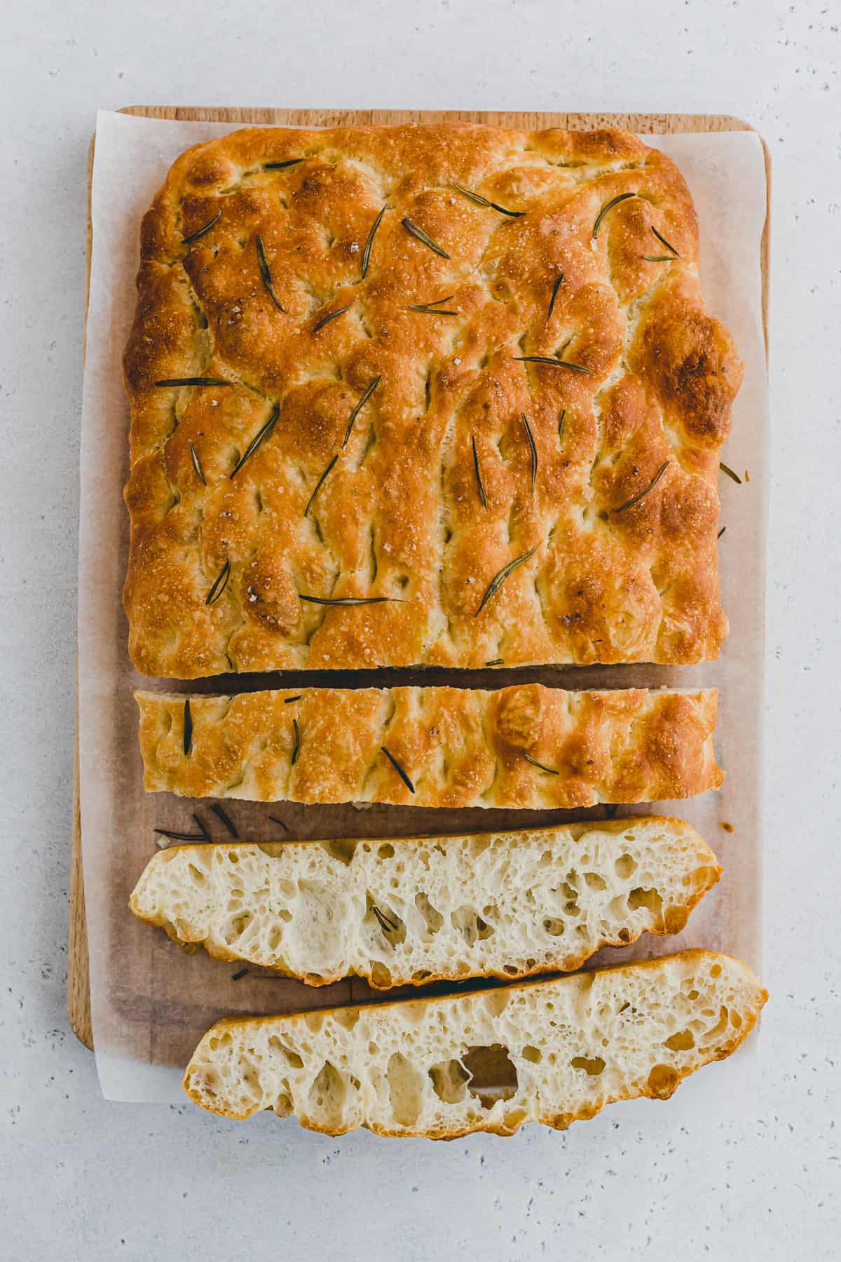 Top view of a rosemary focaccia bread with slices cut out of it, on a chopping board. 