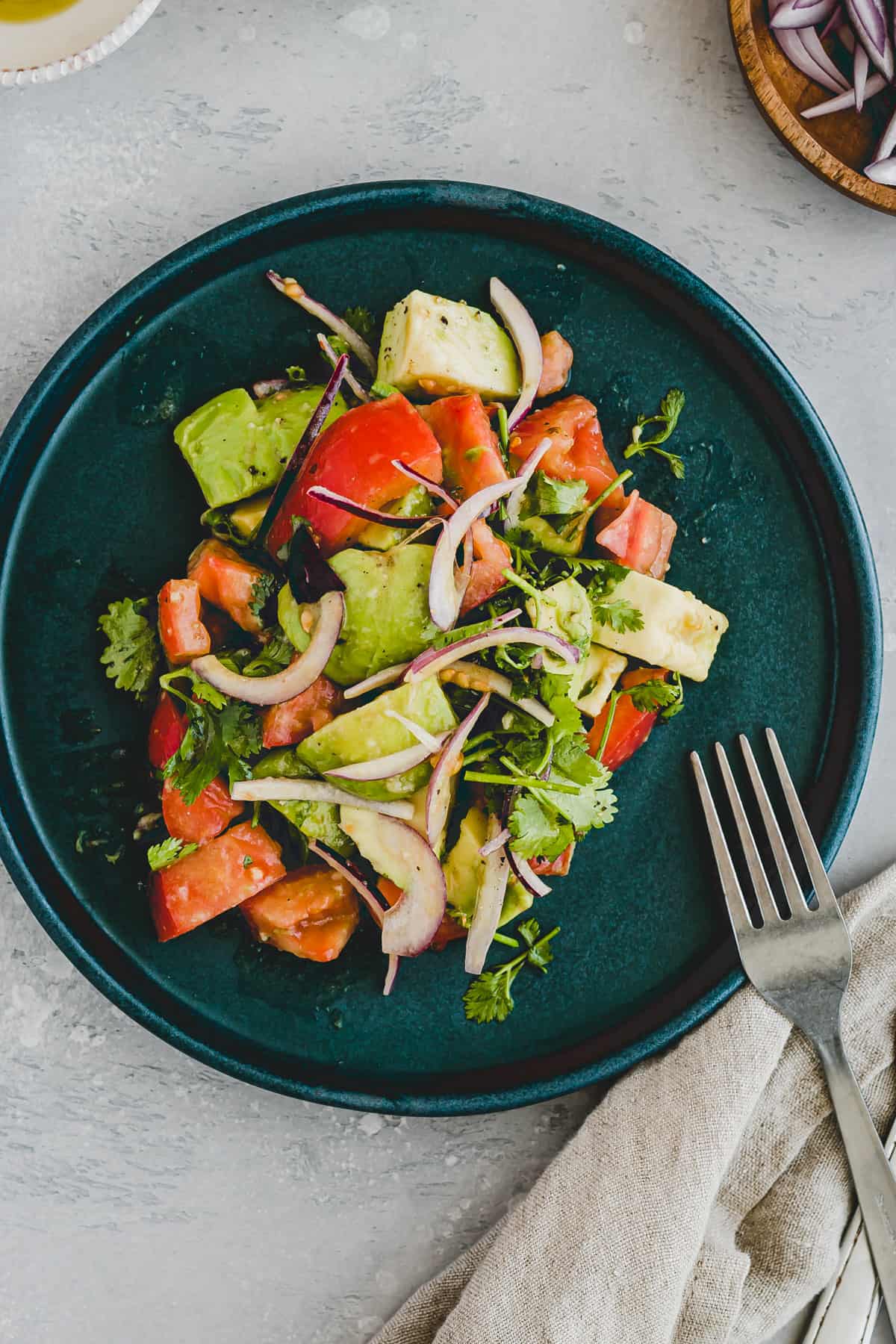 tomato avocado salad with cilantro on a blue plate with a fork