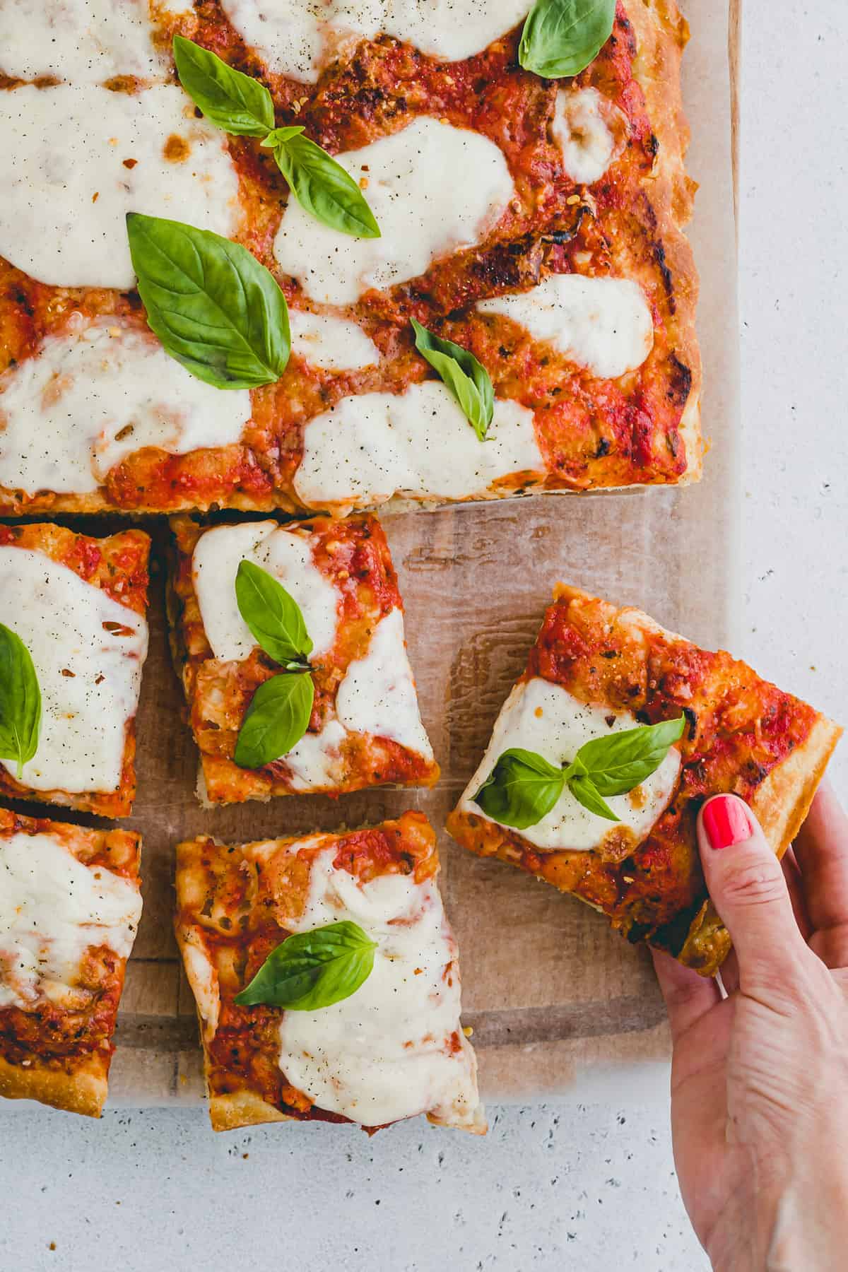 Top view close up of a focaccia pizza cut into slices at the bottom, and a hand is picking up a slice. 