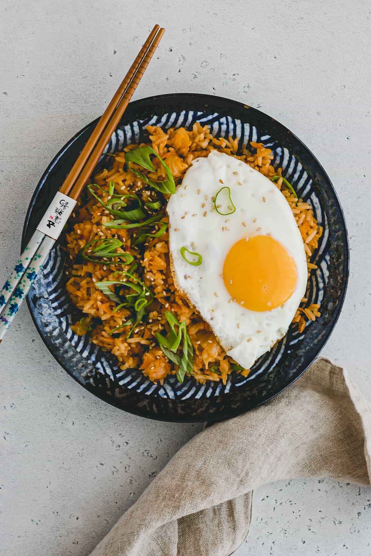 Top view of Kimchi Fried Rice with a fried egg on top on a round blue patterned plate with chopsticks on the side. 