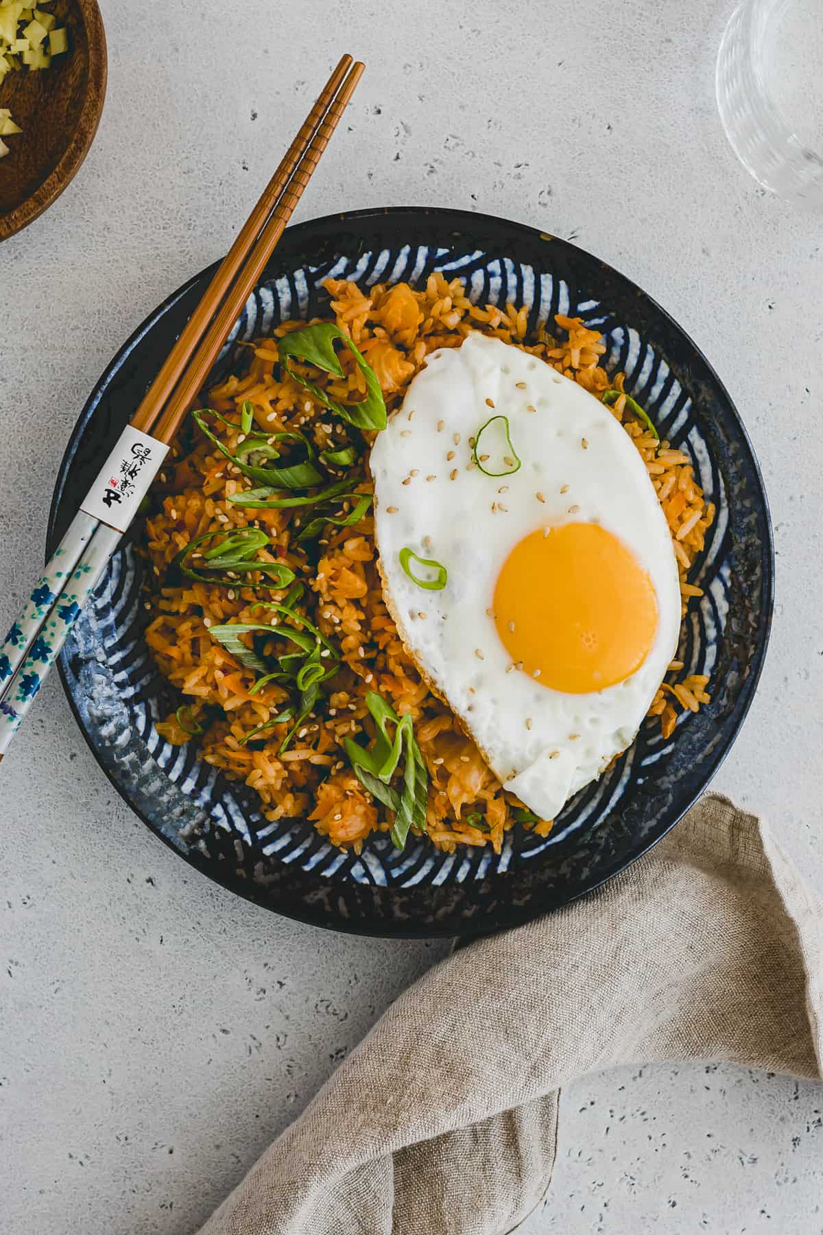 Top view of Kimchi Fried Rice with a fried egg on top on a round blue patterned plate with chopsticks on the side. 