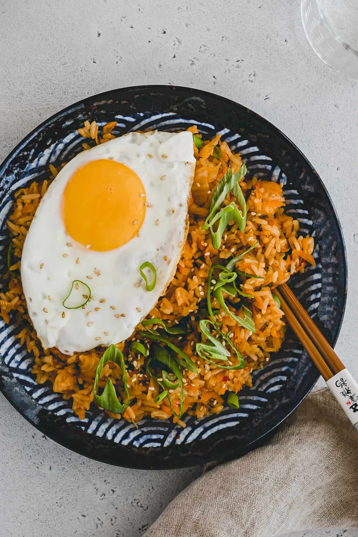 Top view close up of Kimchi Fried Rice with a fried egg on top on a round blue patterned plate with chopsticks on the side. 